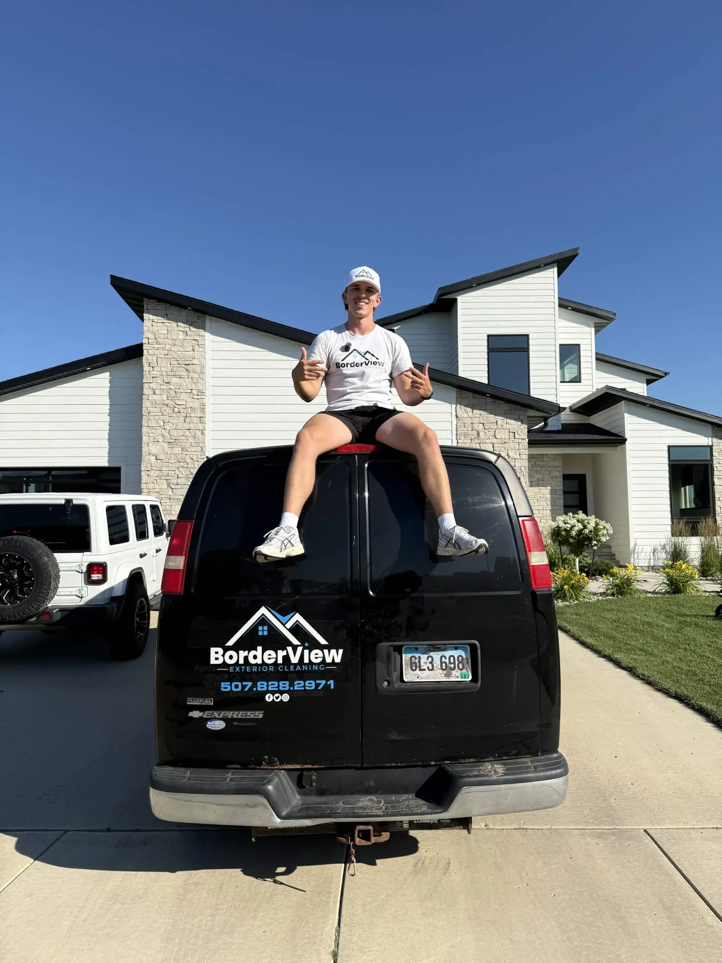 Tate, owner of BorderView Exterior Cleaning, sitting atop the branded service van in front of a freshly cleaned home